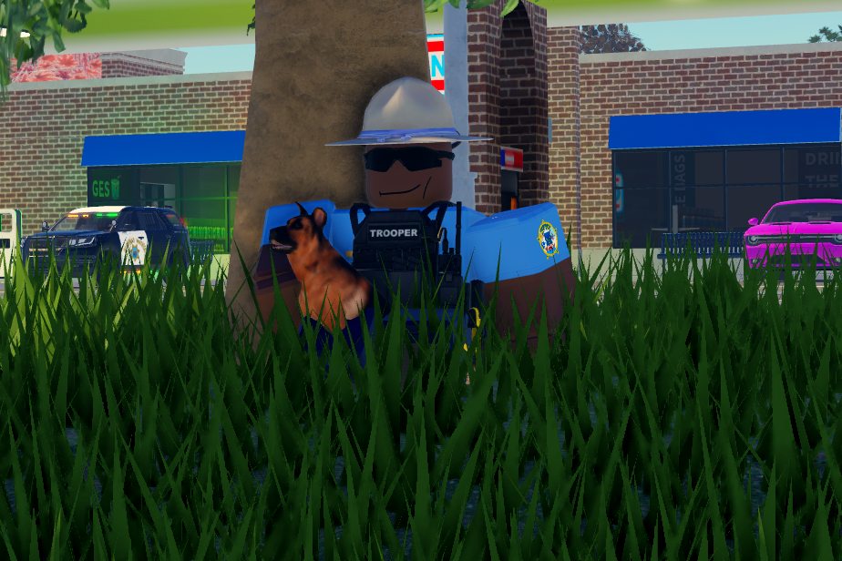 A state trooper and a police dog sitting under a tree by a gas station